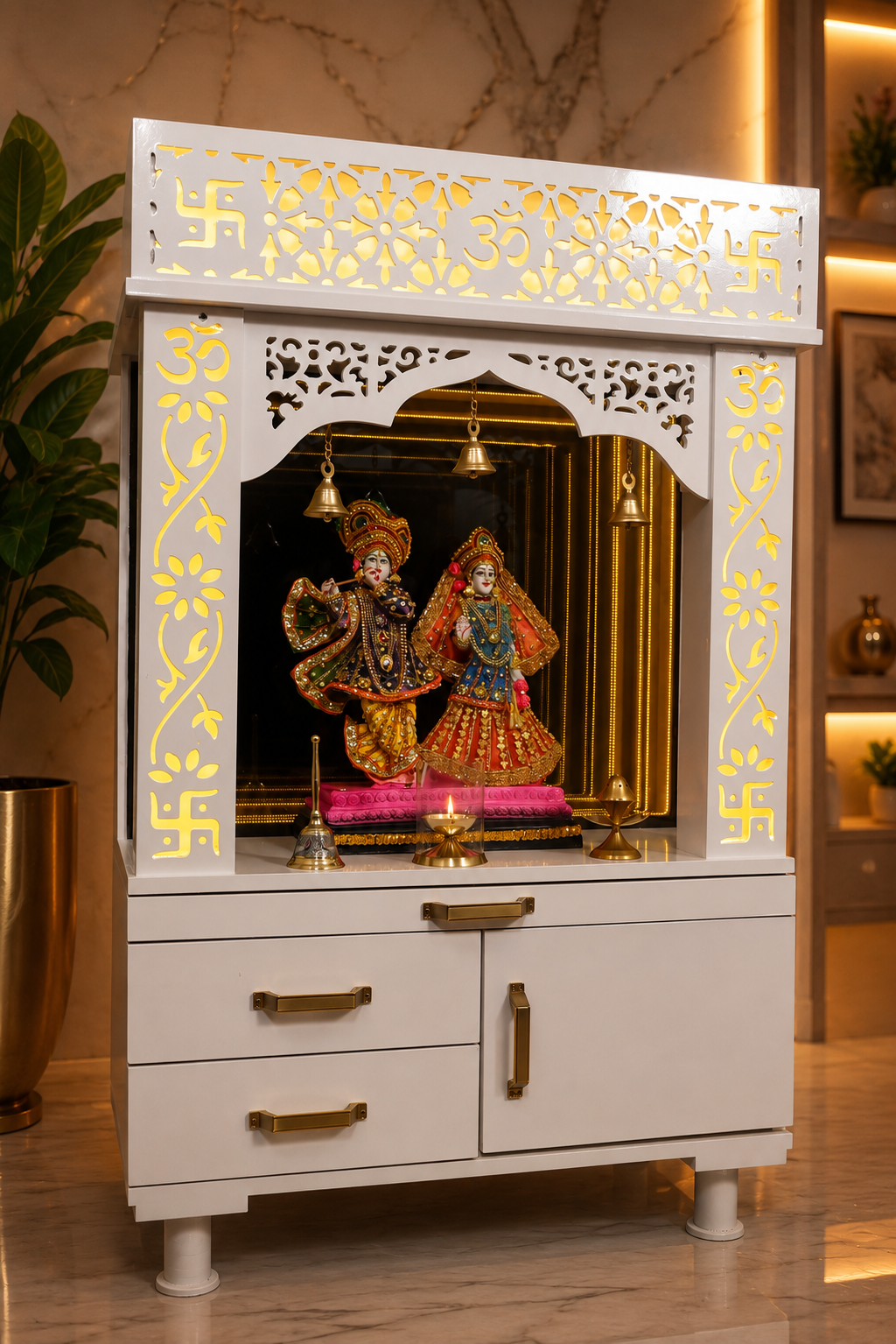 A white wooden Hindu home altar (holy cabinet) with gold accents, featuring a carved swastika at the top, a central arched niche with hanging brass bells, and a deity idol inside, set against a warm, modern home interior background.