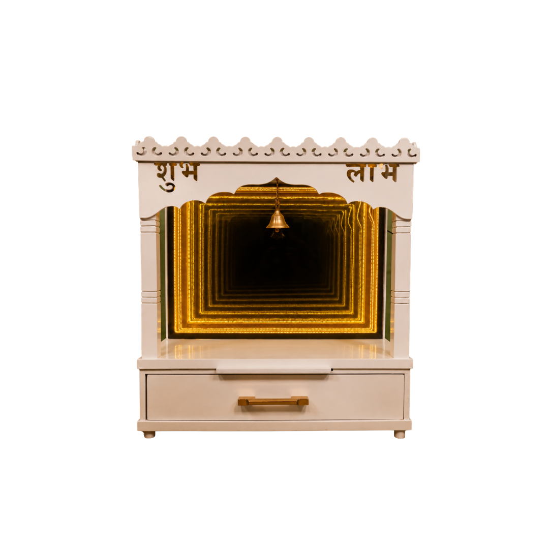 A cream-colored wooden Shubh Lam prayer cabinet with gold accents, featuring a single drawer with a brass handle and a hanging brass bell in the center of the arched opening.