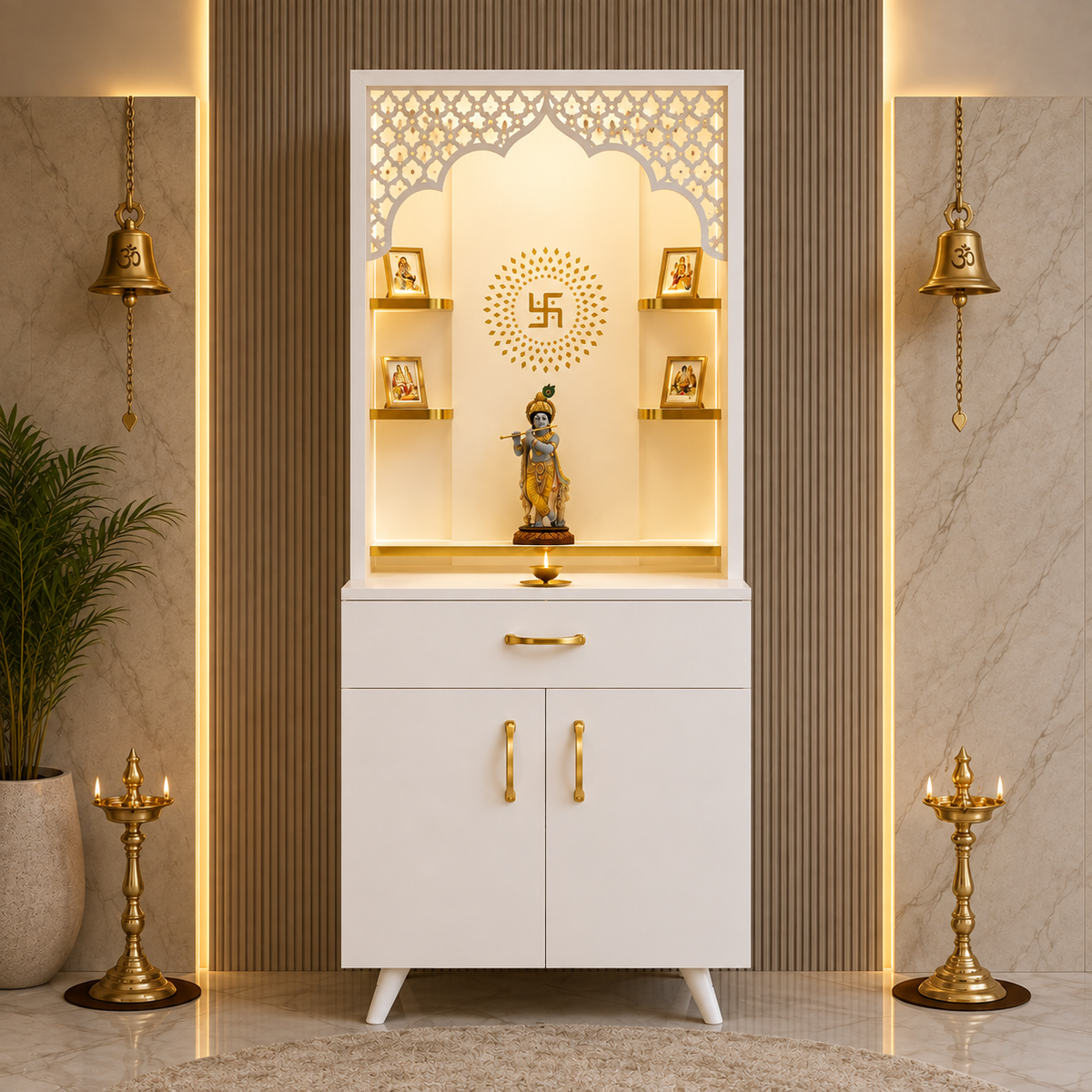 A white and gold Hindu home altar cabinet with a carved arched top panel, built-in shelves, and brass-tone handles and pulls, shown in a styled interior setting with lamps, a plant, and marble walls.