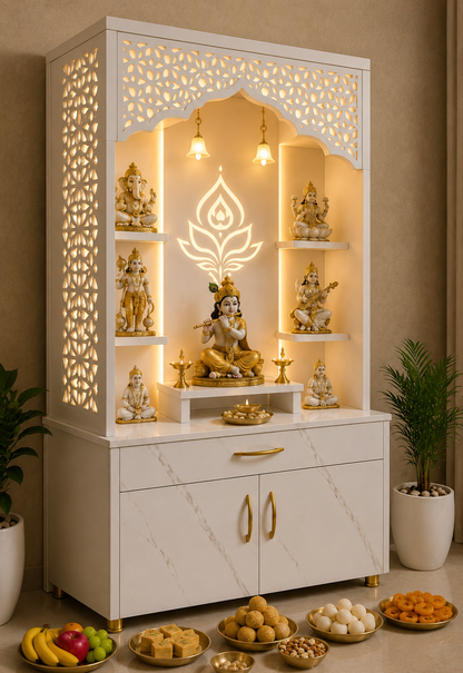 A white and gold Hindu home altar cabinet with illuminated shelves displaying multiple Lord Ganesha statues, set in a decorated room with bowls of food and potted plants.
